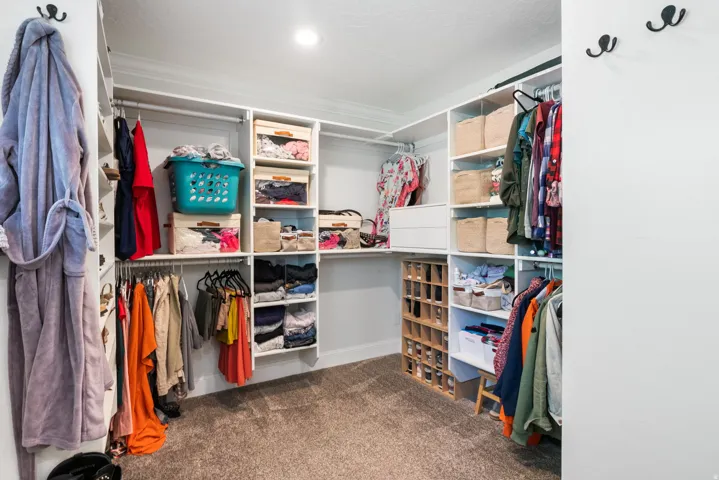 Walk-in closet featuring built-in white shelving, multiple hanging rods, dedicated shoe storage, and soft carpet flooring