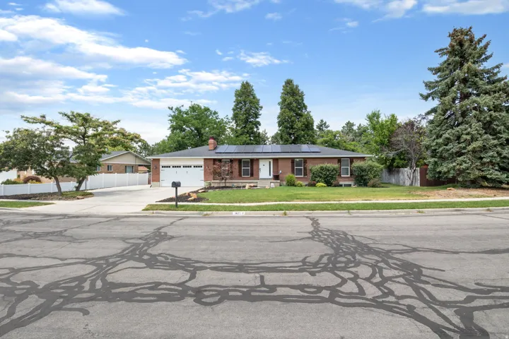 Brick exterior ranch-style residence featuring solar panels, a two-car garage, and a concrete driveway