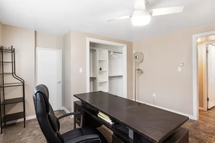 Carpeted interior space featuring a ceiling fan with integrated lighting, a built-in closet system with shelving, and a white interior door