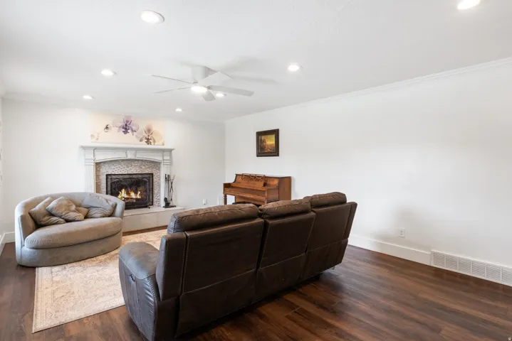 Living area featuring a detailed fireplace with a decorative mantel and hearth, wood-finish flooring, ceiling fan, recessed lighting, and crown molding