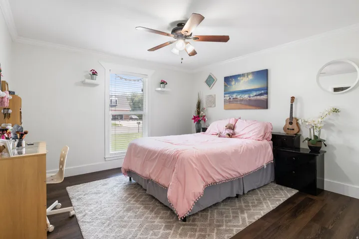 Well-lit room featuring dark wood-finish flooring, white baseboards, and crown molding