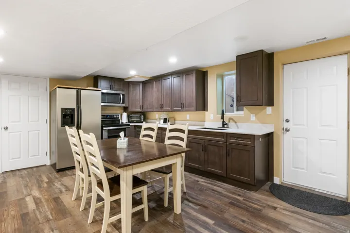 Kitchenette featuring wood-finish flooring, dark wood cabinetry, white countertops, and stainless steel appliances