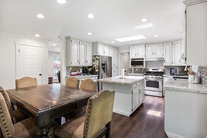 Kitchen featuring wood-finish flooring, white cabinetry, granite countertops, a central island, and stainless steel appliances