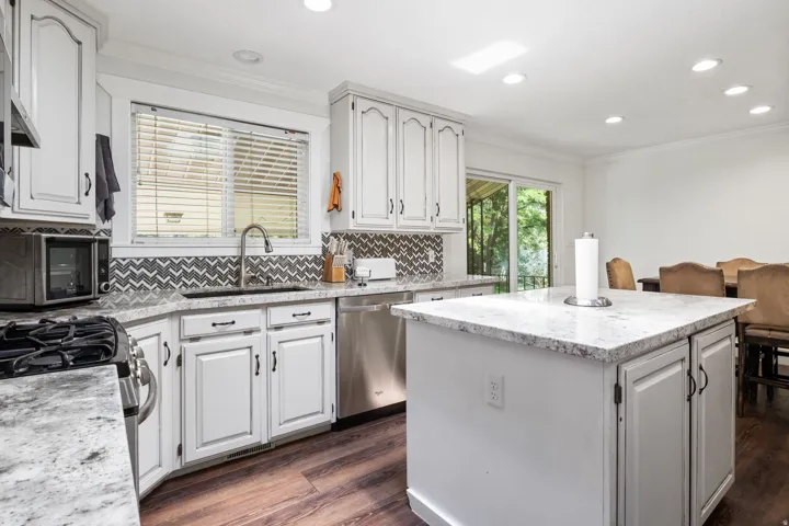 Bright kitchen featuring white cabinetry, granite-finish countertops, stainless steel appliances, a chevron-patterned backsplash, and wood-finish flooring
