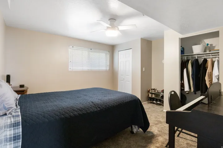 Bedroom featuring neutral wall paint, a window with horizontal blinds, carpeted flooring, a ceiling fan with light, and an open closet with shelving and hanging rods