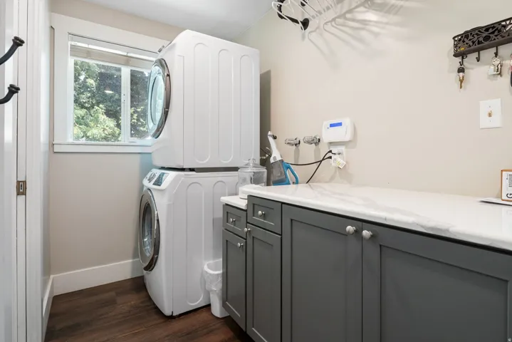 Laundry area featuring stacked appliances, dark wood-finish flooring, a white countertop, and grey cabinetry