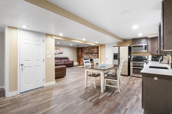 Open-concept lower level featuring durable wood-finish flooring, recessed lighting, a full kitchen with stainless steel appliances and dark cabinetry, and a stone accent wall