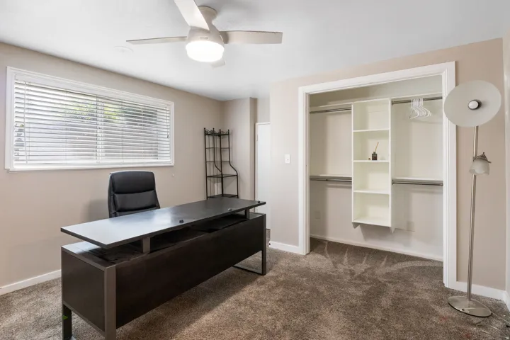 Room featuring a ceiling fan with integrated lighting, a window with horizontal blinds, neutral wall paint, and a built-in closet organization system