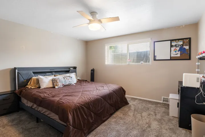 Spacious carpeted room featuring a ceiling fan with integrated lighting, a large window with horizontal blinds, and neutral wall tones