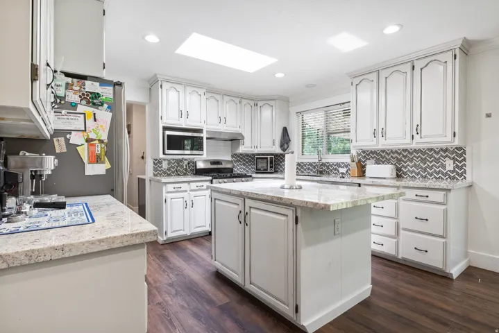 Kitchen featuring a central island with a stone-finish countertop, white cabinetry, dark wood-finish flooring, a patterned tile backsplash, and a skylight