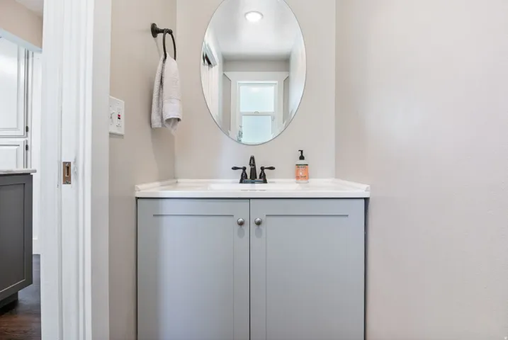 Bathroom vanity featuring a light gray cabinet with brushed nickel hardware, white countertop, and an oval mirror