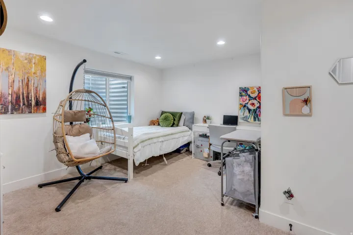Recessed lighting illuminates this bright room featuring neutral-toned carpeting, white baseboards, and a window with horizontal blinds