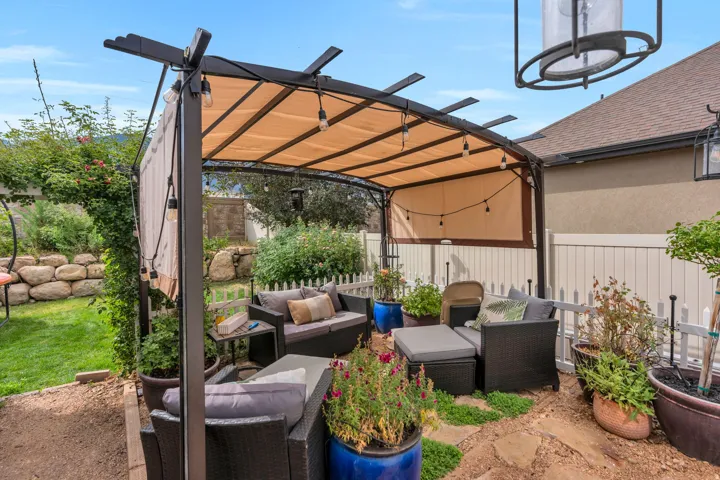 Patio featuring a large pergola with a retractable canopy, string lighting, irregular flagstone paving, and a white picket fence