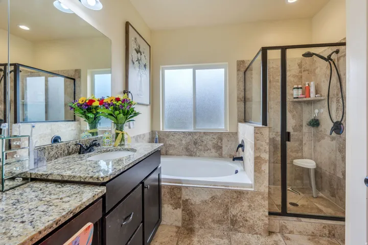 Bathroom featuring a large soaking tub, separate glass-enclosed shower, dual-sink vanity with granite countertop, and tiled flooring