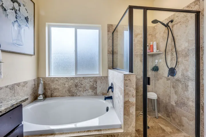 Spacious bathroom featuring a built-in soaking tub with a dark bronze faucet, a frosted window, and a separate shower enclosure with a dark bronze frame