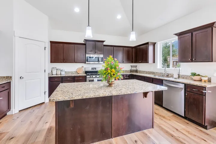 Kitchen featuring a central island with a light-colored countertop, dark wood-finish cabinetry, stainless steel appliances, light wood-finish flooring, and pendant lighting