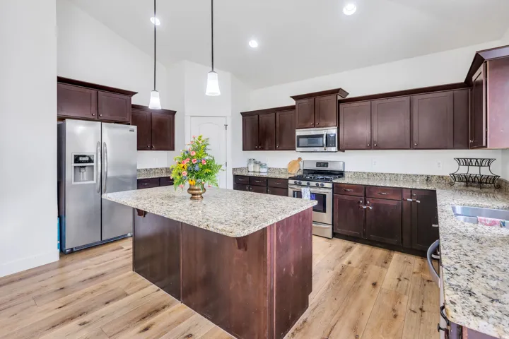 Kitchen featuring an island with granite countertop, stainless steel appliances, dark wood cabinetry, wood-finish flooring, and pendant lighting