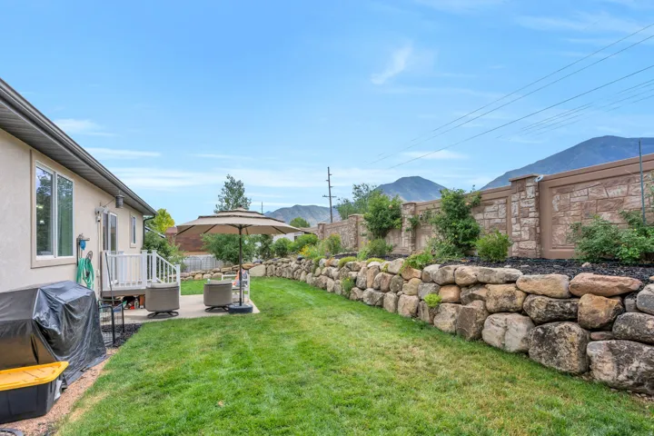 Expansive backyard featuring a manicured lawn, a stone retaining wall, and a concrete patio