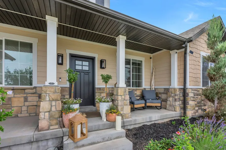 Covered front porch featuring stacked stone accents and a black entry door with transom windows