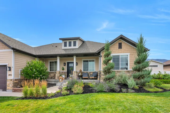 Craftsman-style exterior featuring a covered front porch, stone and siding façade, dormer window, and mature landscaping