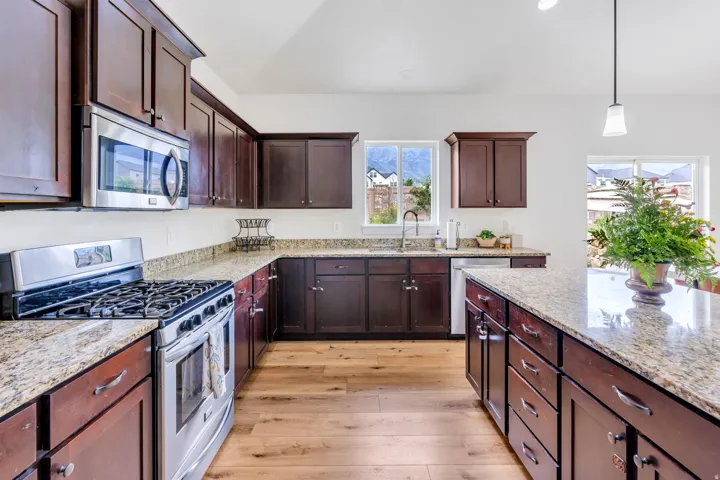 Kitchen featuring dark wood cabinetry, granite countertops, stainless steel appliances, a center island with additional storage, and wood-finish flooring