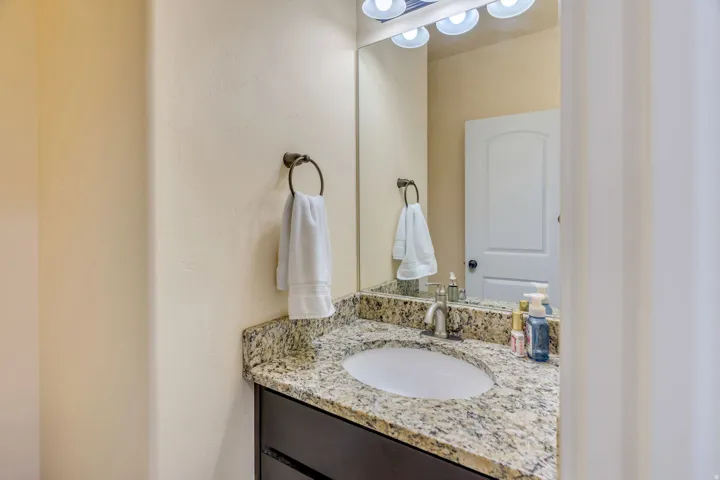 Bathroom vanity featuring a granite countertop with an undermount sink, brushed nickel faucet, dark wood-finish cabinetry, and overhead lighting fixture