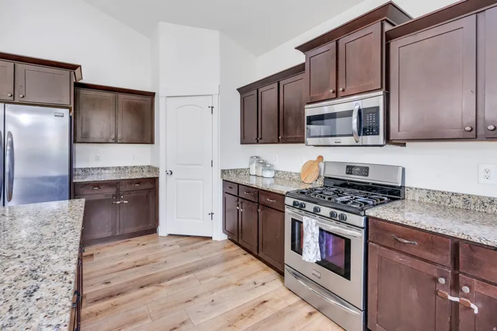 Kitchen featuring wood-finish flooring, dark wood cabinetry, granite-style countertops, and stainless steel appliances including a refrigerator, range, and microwave