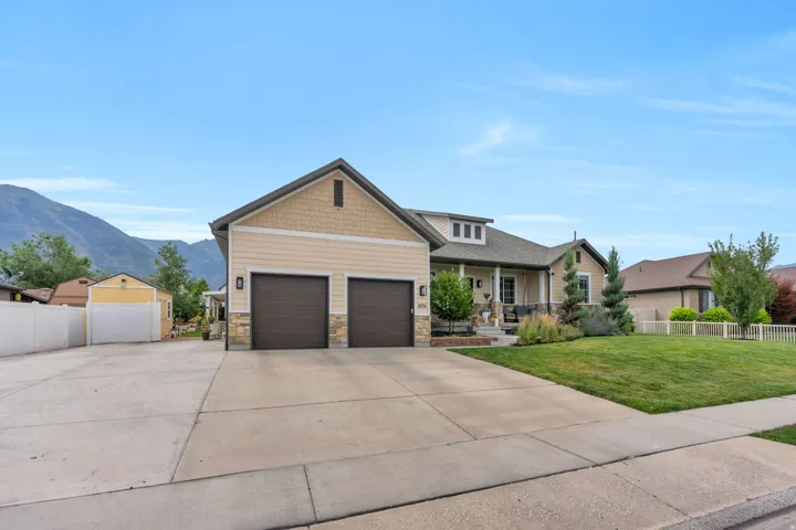 Ranch-style residence featuring a two-car garage, expansive concrete driveway, and a covered front porch with stone accents