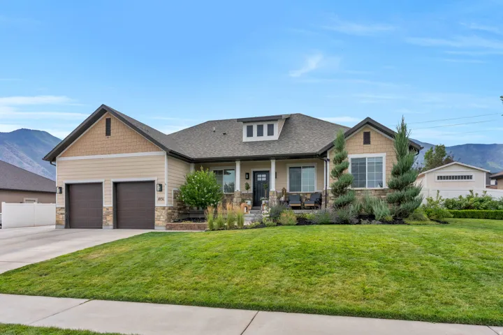 Contemporary ranch-style residence featuring a two-car garage, stone and siding facade, covered front porch, and dormer windows