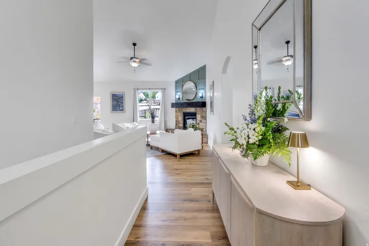 Open-concept interior featuring wood-finish flooring, a stone fireplace with a dark wood mantel, and an arched entryway