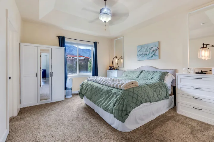 Expansive bedroom featuring textured carpet flooring, a tray ceiling with a ceiling fan, and a large window