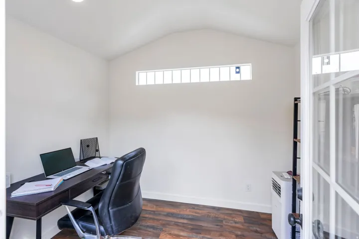 Vaulted ceiling interior with wood-finish flooring, white walls, and a transom window