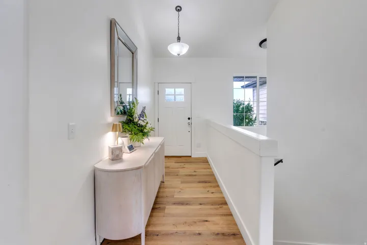 Bright entryway featuring wood-finish flooring, a white paneled door with glass inserts, and a white balustrade