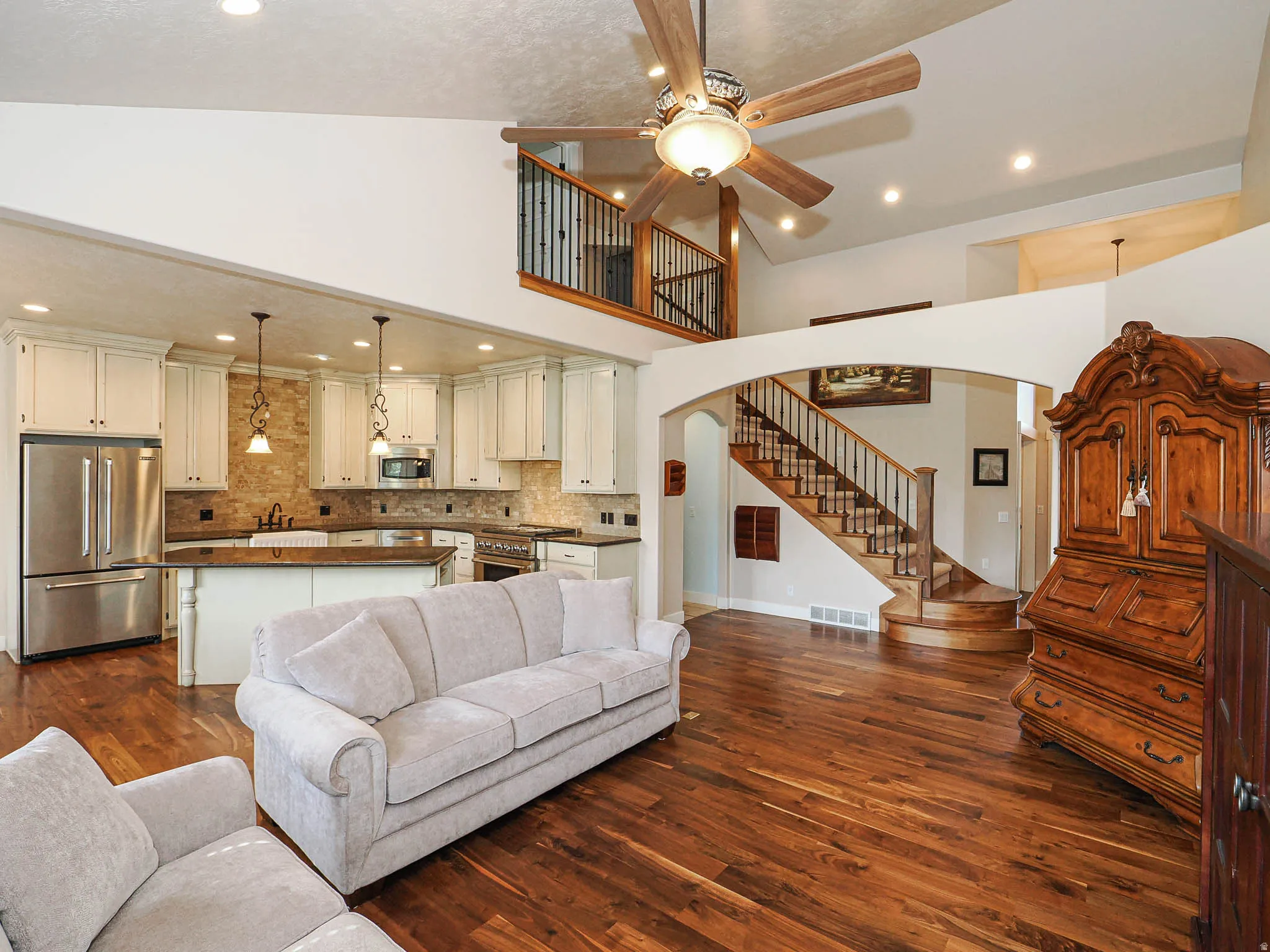Open-concept living space with vaulted ceilings, rich wood-finish flooring, and a kitchen featuring white cabinetry, stone backsplash, and stainless steel appliances