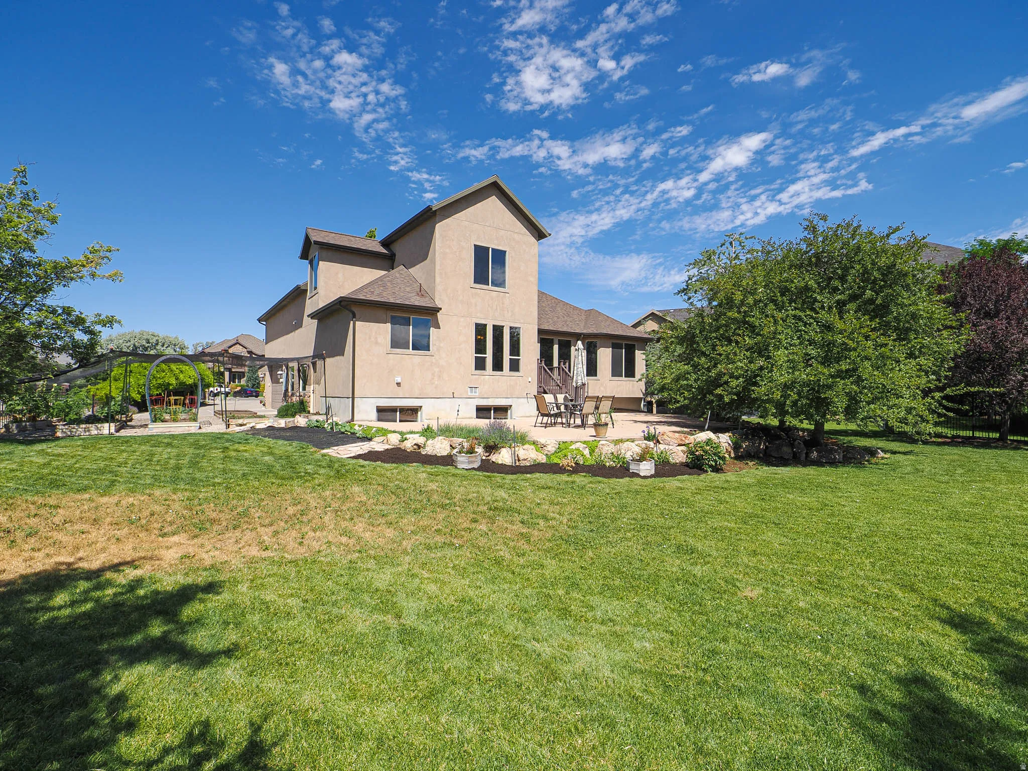 Expansive backyard featuring a manicured lawn, a large stone patio, and mature trees