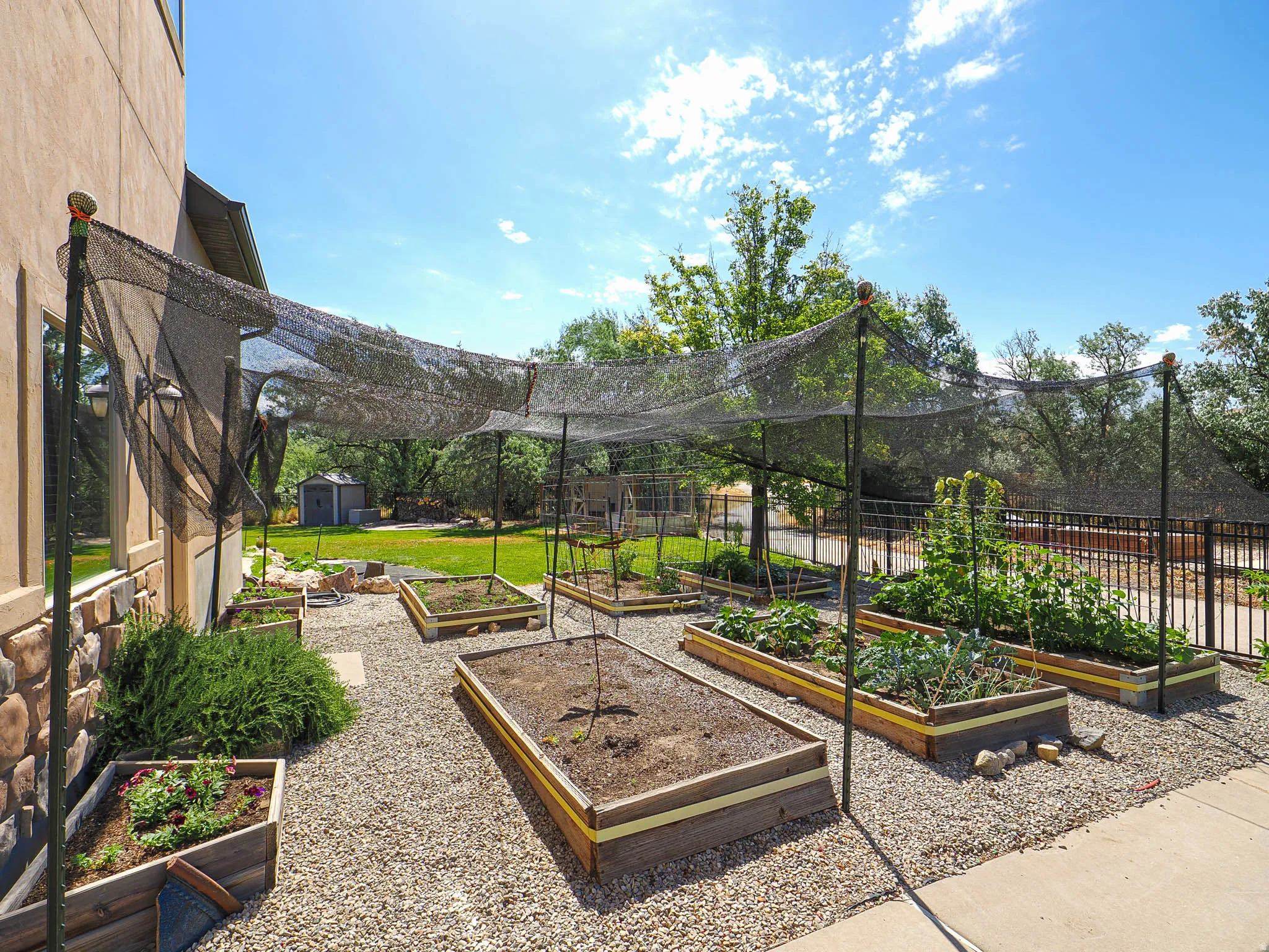 Outdoor garden area featuring multiple raised garden beds, gravel pathways, and a black mesh shade structure