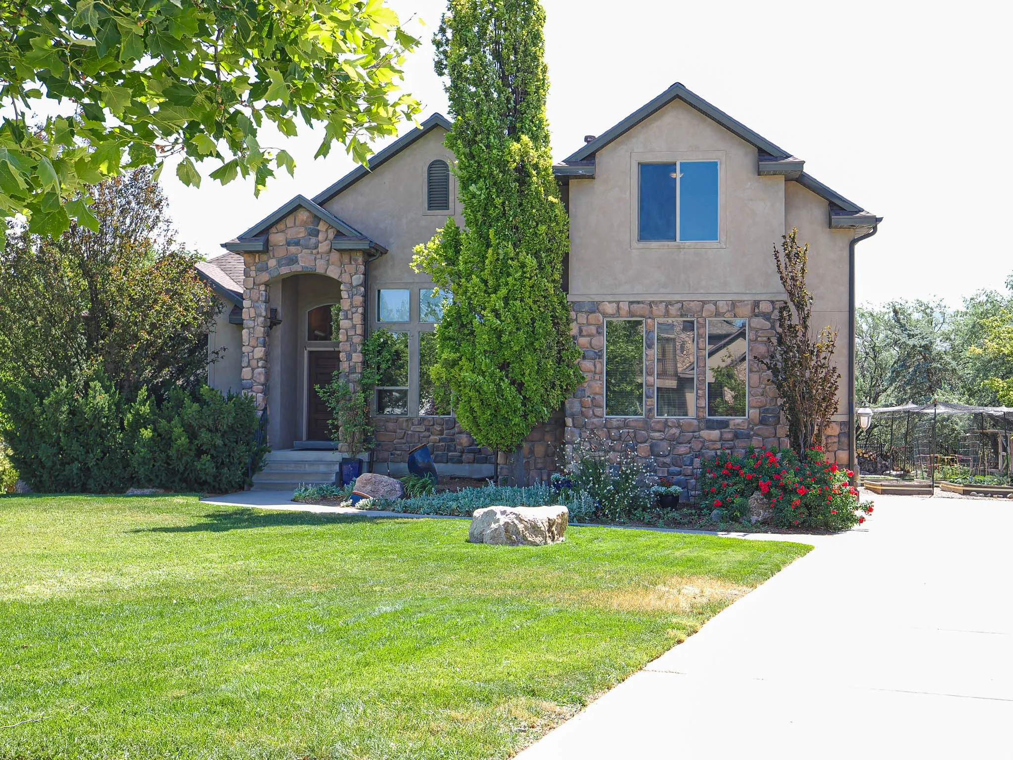 Stucco and stone facade home featuring an arched entryway, multiple window styles, established landscaping, and a concrete driveway