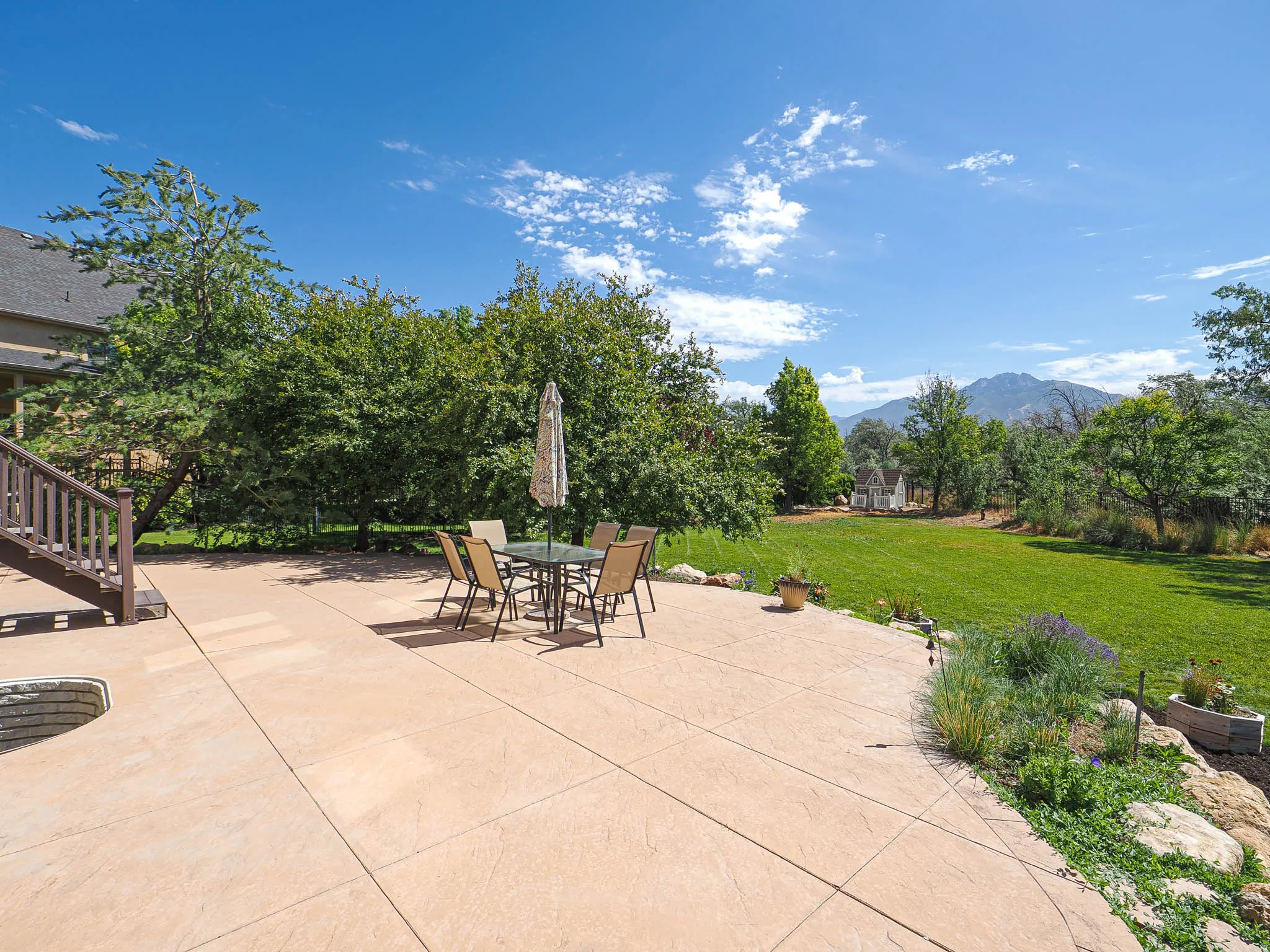 Expansive stamped concrete patio with stone retaining walls, integrated fire pit, and staircase access