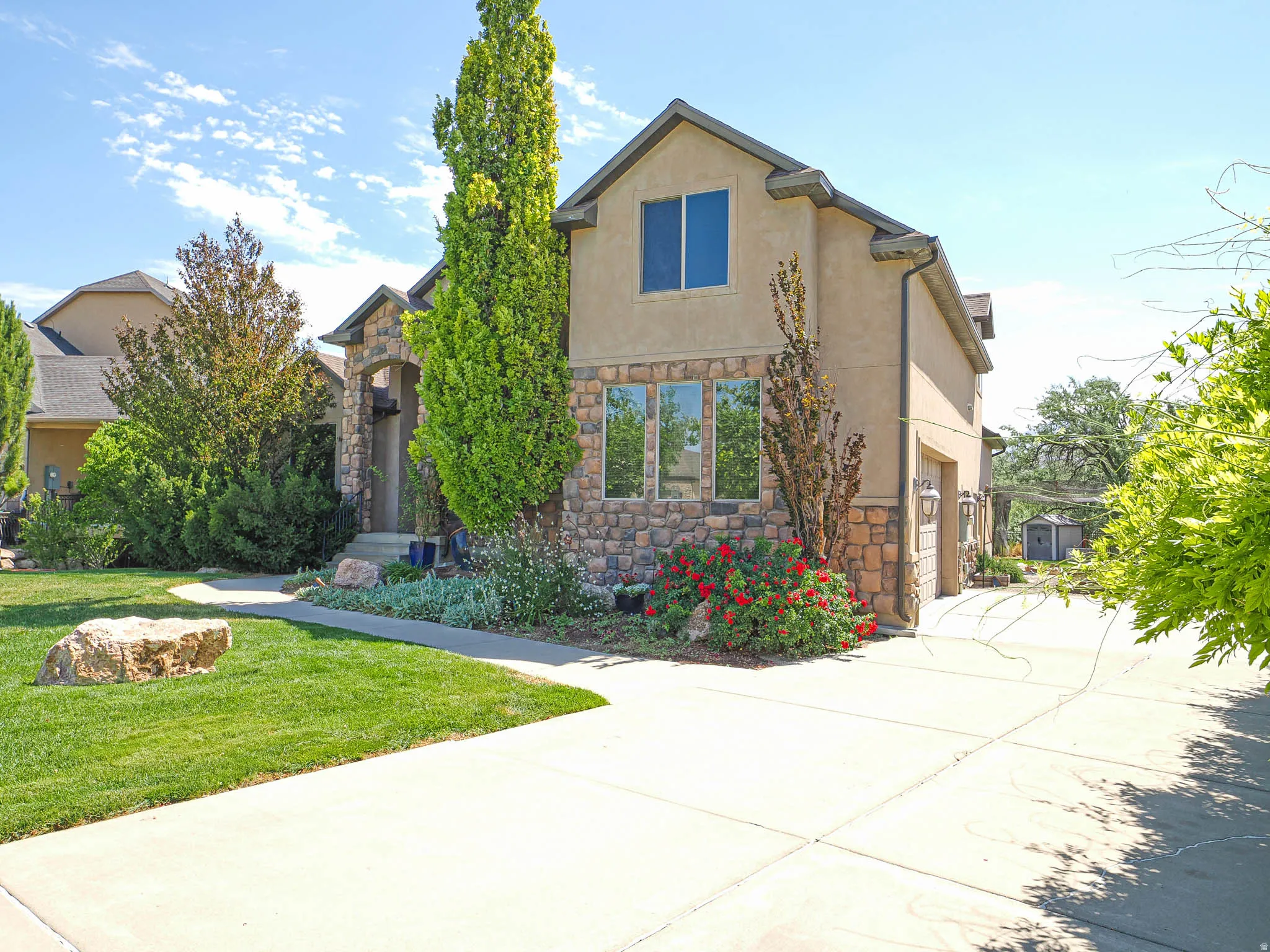 Stucco and stone exterior featuring an arched entry, expansive driveway, established landscaping, and an attached garage