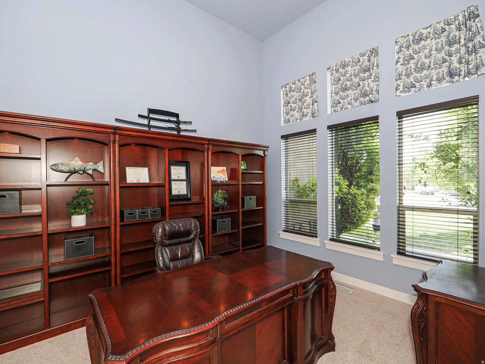 Office space featuring extensive built-in wooden shelving, a large ornate wooden desk, and three tall windows with privacy blinds