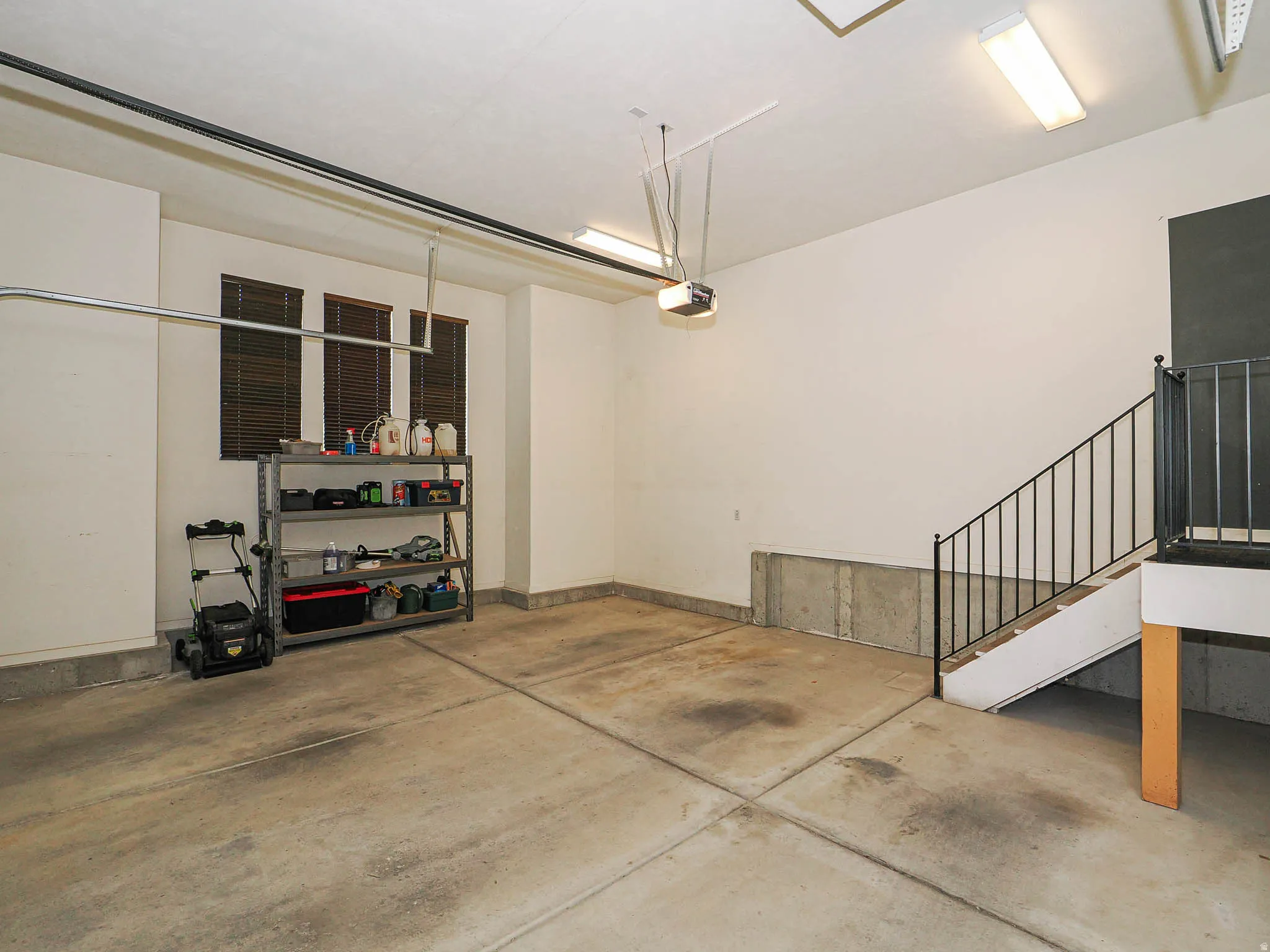 Spacious garage with concrete flooring, multiple windows featuring blinds, and an interior staircase with metal railings