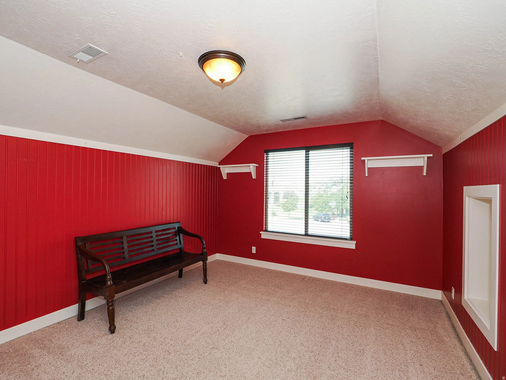 Carpeted room featuring a window with horizontal blinds, sloped ceilings, and red beadboard paneling