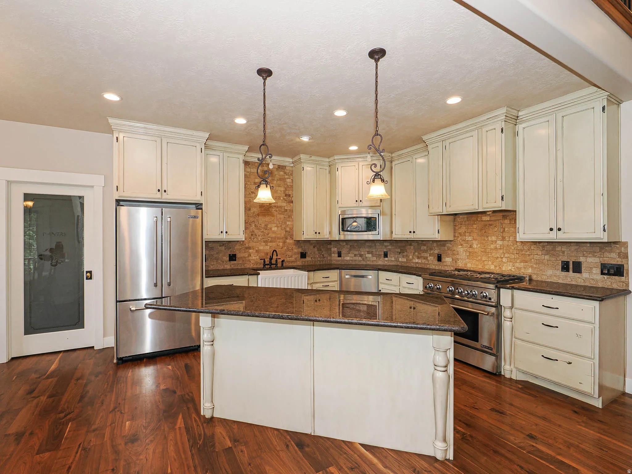 Kitchen featuring wood-finish flooring, an expansive center island with granite countertop, stainless steel appliances, abundant cabinetry, and a stone-tiled backsplash