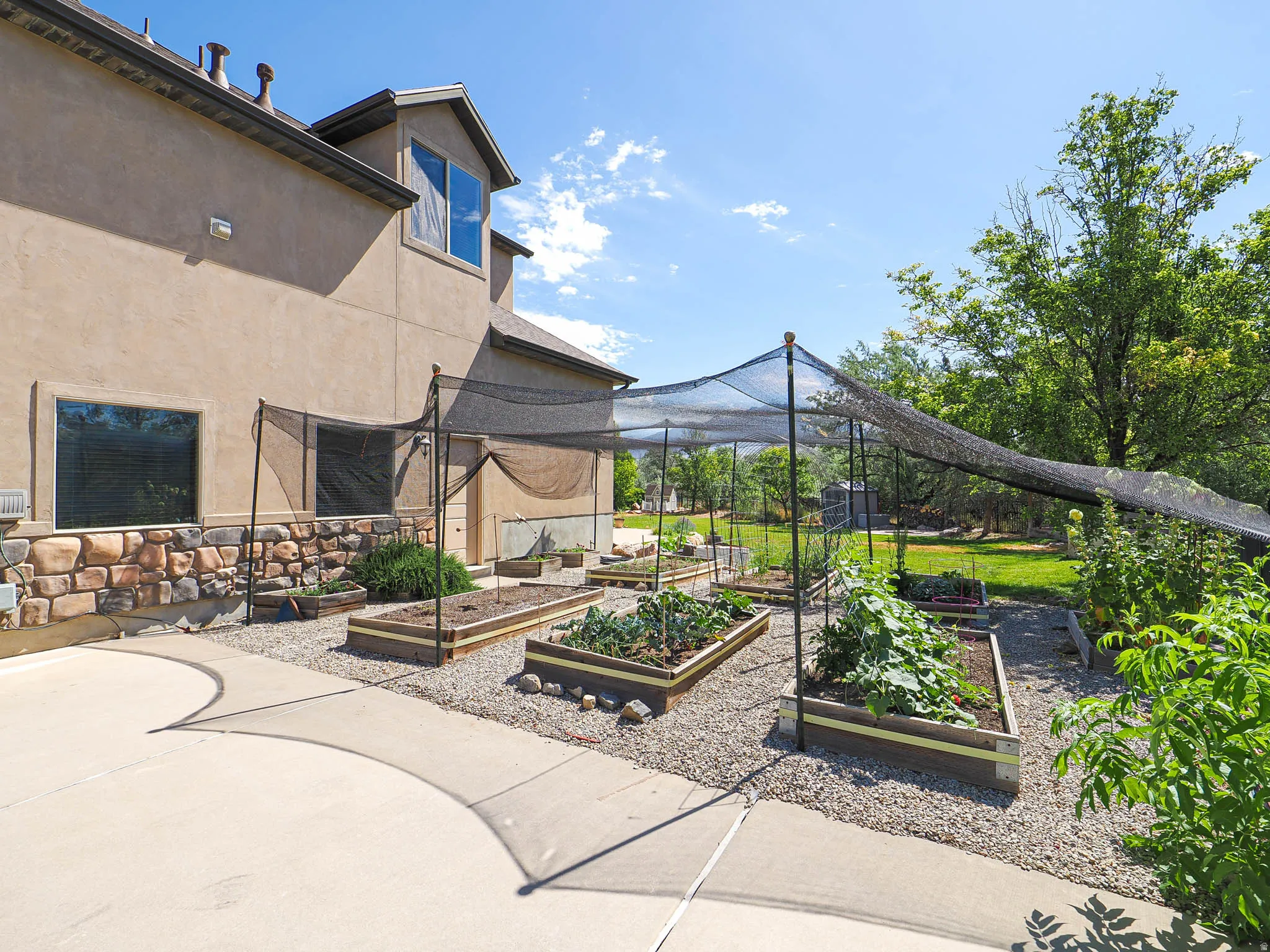 Exterior rear of the property featuring multiple raised garden beds under a shade canopy