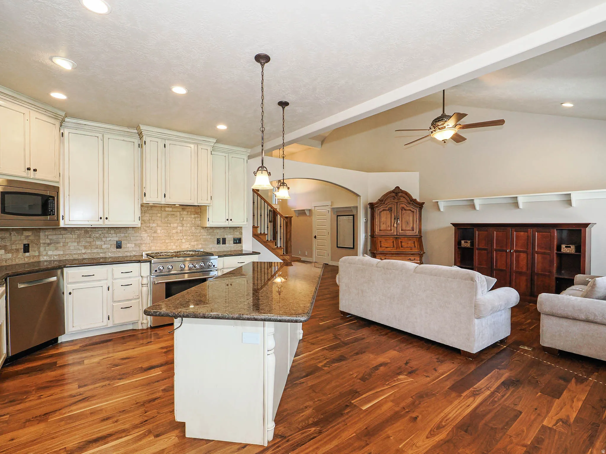 Open-concept kitchen and living area featuring wood-finish flooring, white cabinetry, a large kitchen island with pendant lighting, stainless steel appliances, and vaulted ceilings