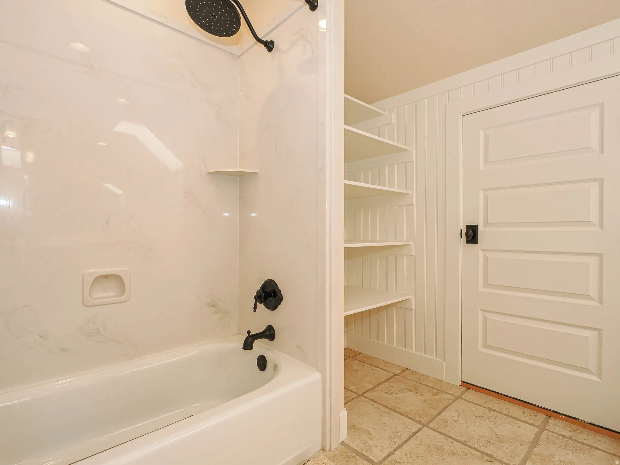Bathtub with matte black fixtures and a rain shower head, complemented by a white marble-patterned shower surround
