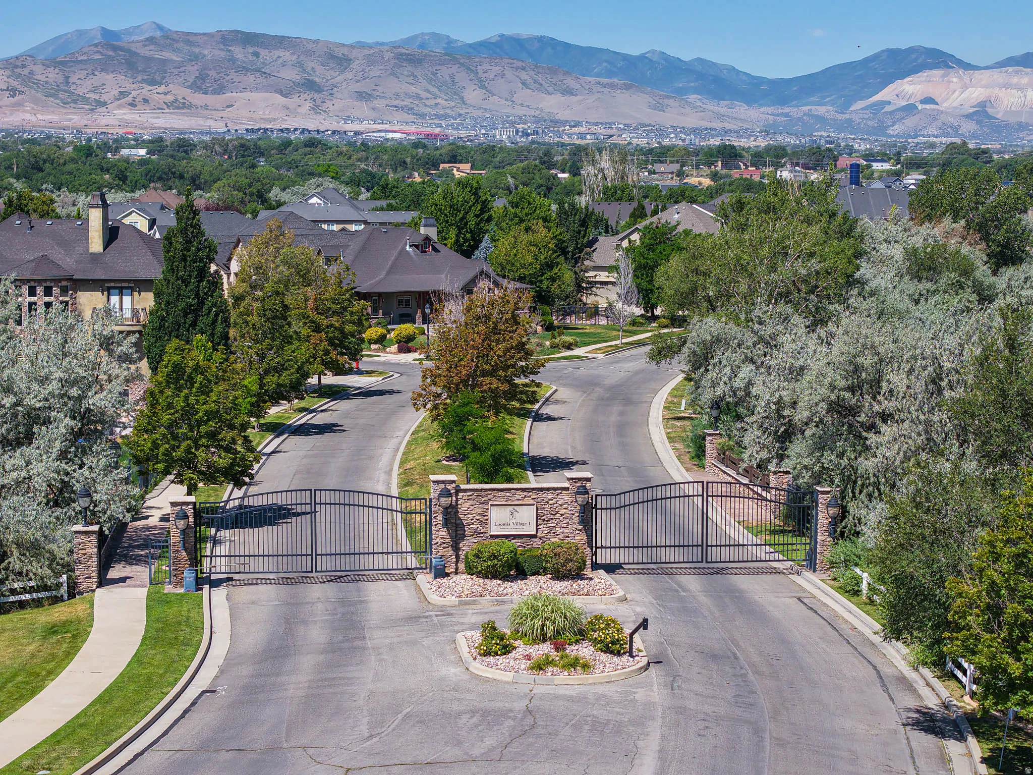 Gated community entry with stone pillars, wrought iron gates, and mature landscaping