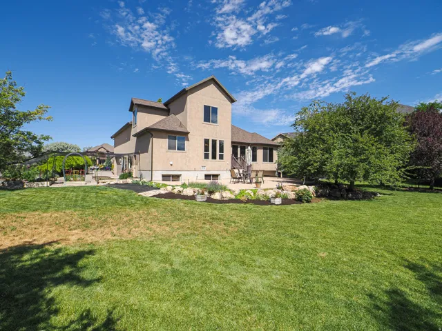 Expansive backyard featuring a manicured lawn, a large stone patio, and mature trees
