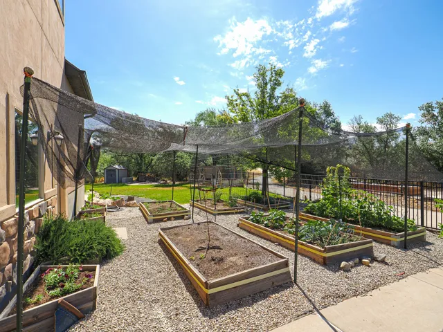 Outdoor garden area featuring multiple raised garden beds, gravel pathways, and a black mesh shade structure