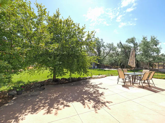 Expansive outdoor patio featuring large square-cut concrete pavers, surrounded by mature trees and verdant green lawn